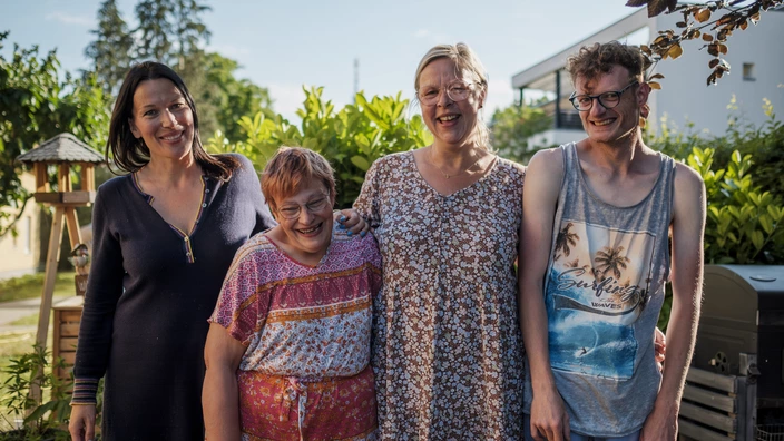 Zwei Erzieherinnen stehen gemeinsam mit einer Frau mit Behinderung und einem Mann mit Behinderung im Garten ihrer Wohnstätte.