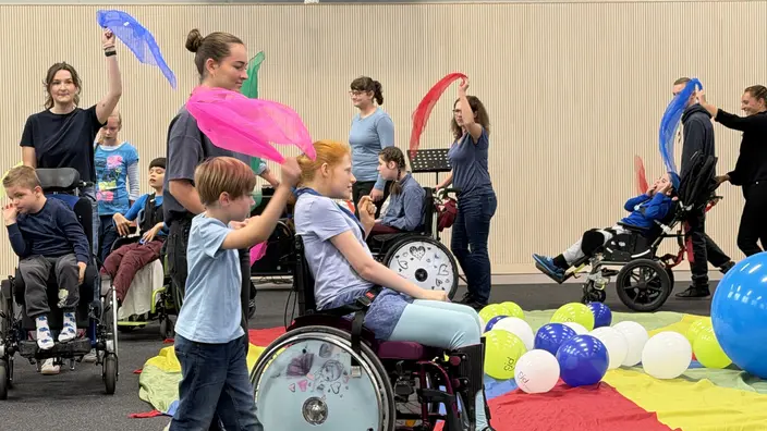 Schüler im Rollstuhl und Pädagogen mit bunten Tüchern